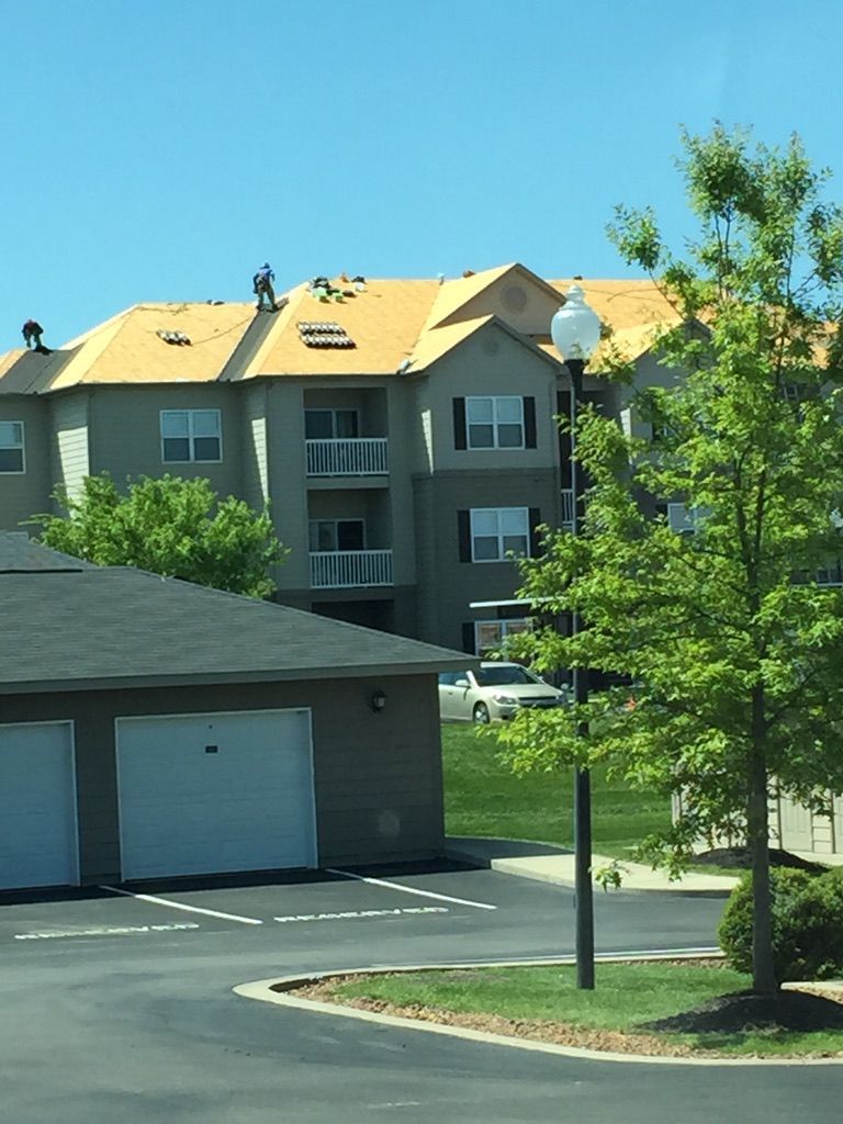 Apartment building with roofers working on the roof under a blue sky. A garage is in the foreground.