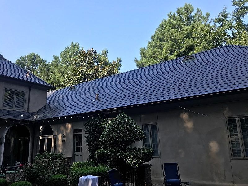 A large house with a slate roof is surrounded by trees and bushes.