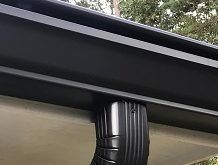 A close up of a black gutter on a roof with trees in the background.