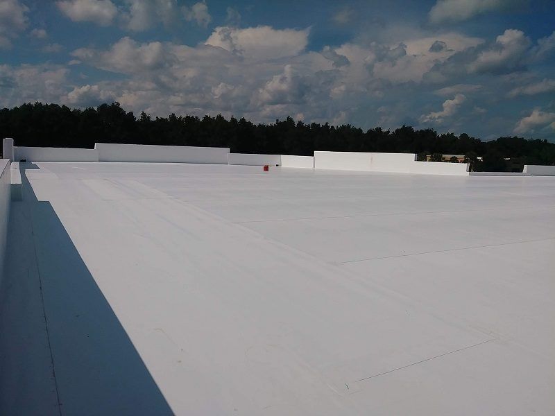 A large white roof with trees in the background on a sunny day.