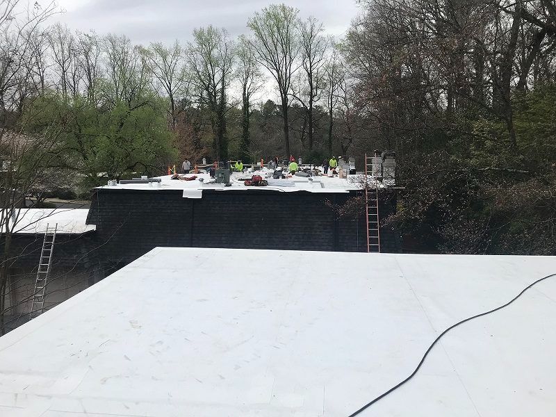 A white roof is being installed on a building with trees in the background.