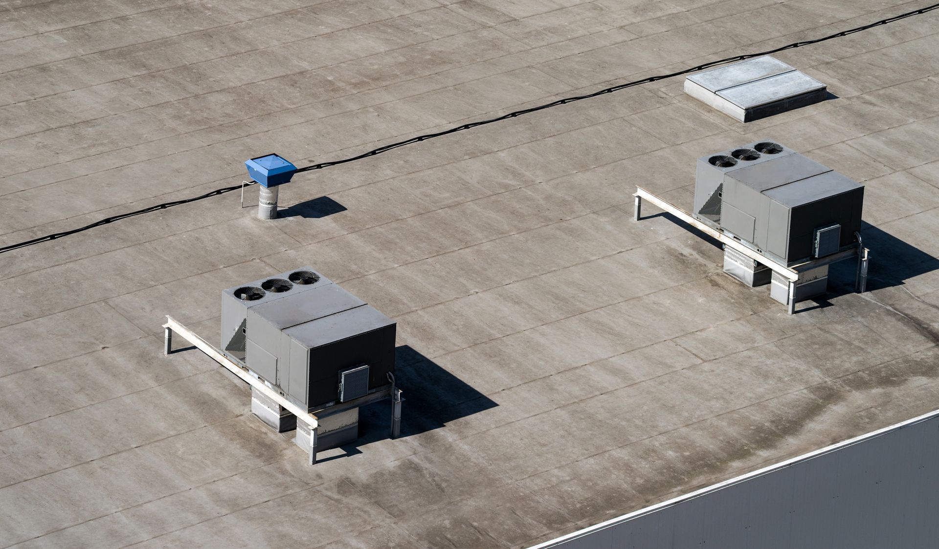 Three air conditioners are sitting on top of a concrete roof.