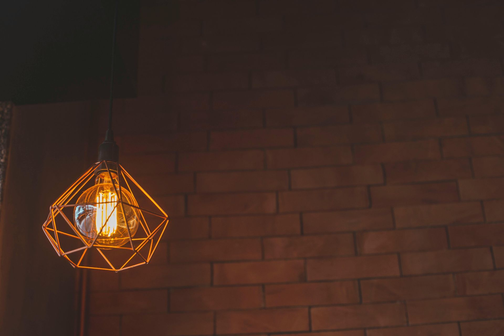 Geometric pendant lamp illuminating a brick wall.