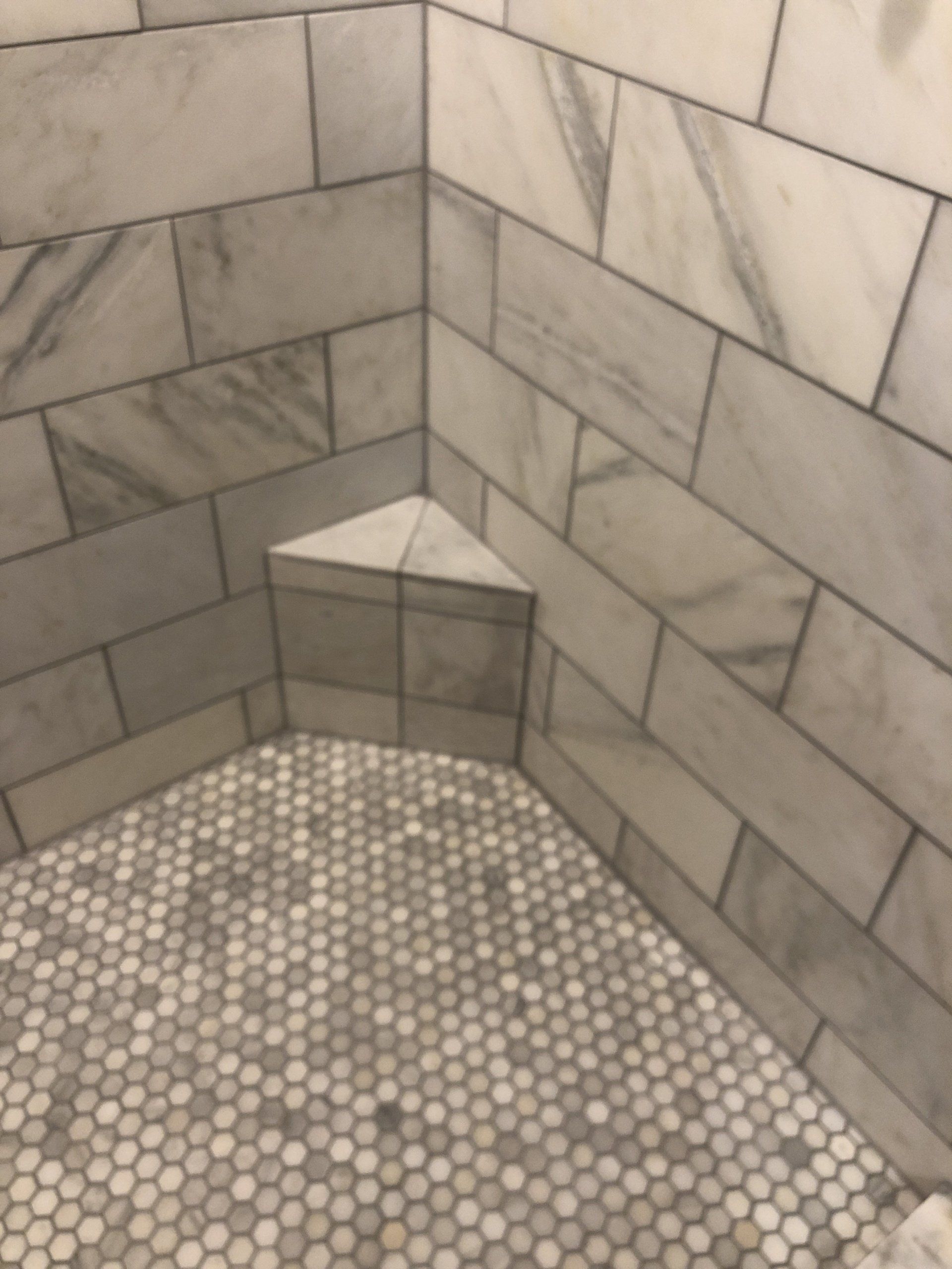 A shower with white tiles and a corner seat
