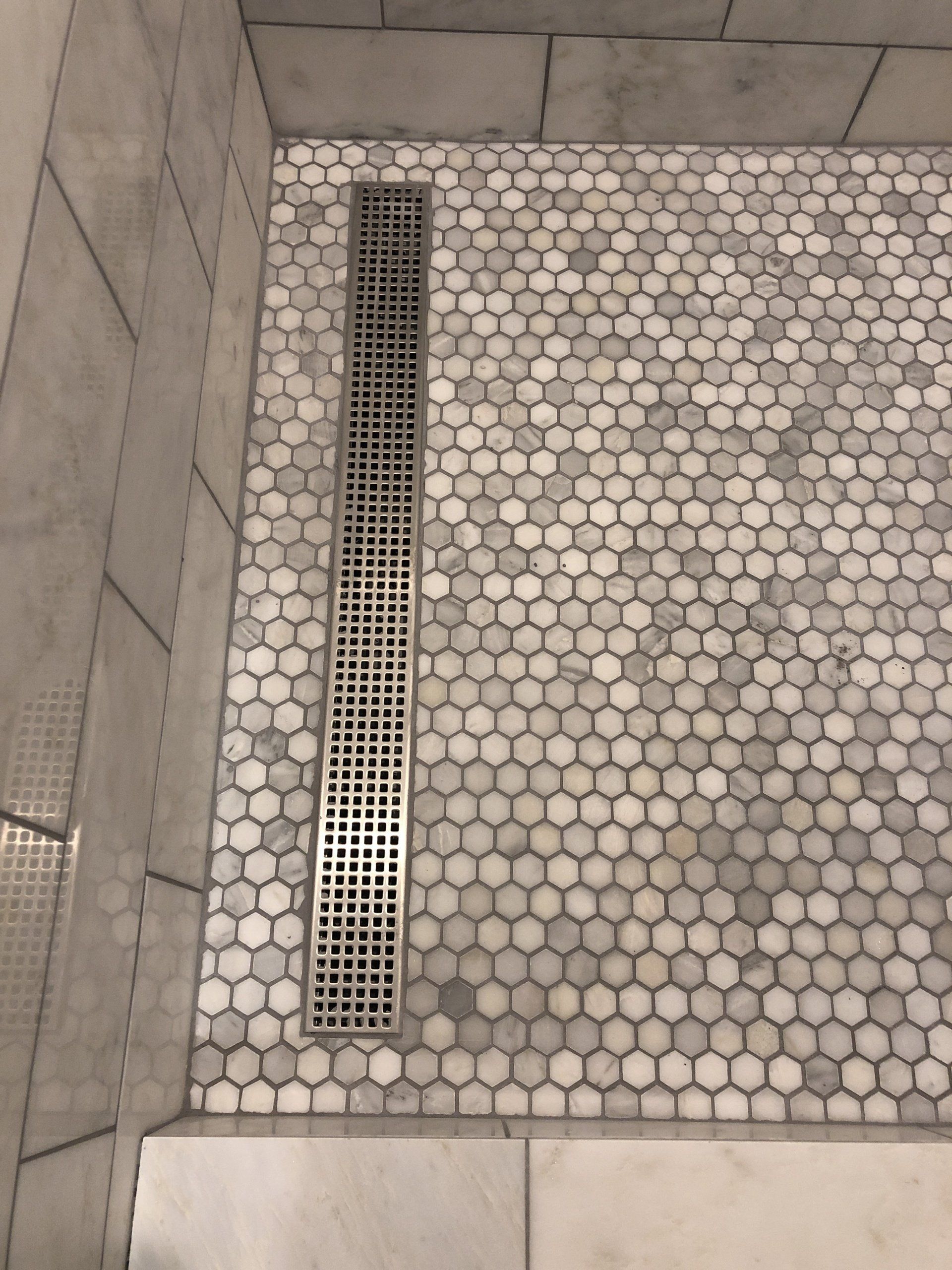 A shower with white tiles and a drain on the floor