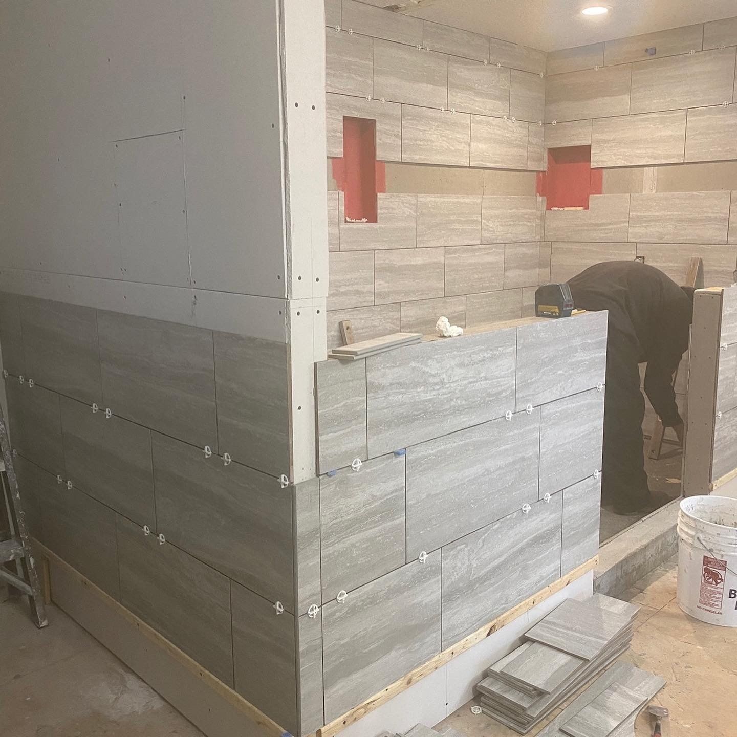A man is laying tiles on a wall in a room.