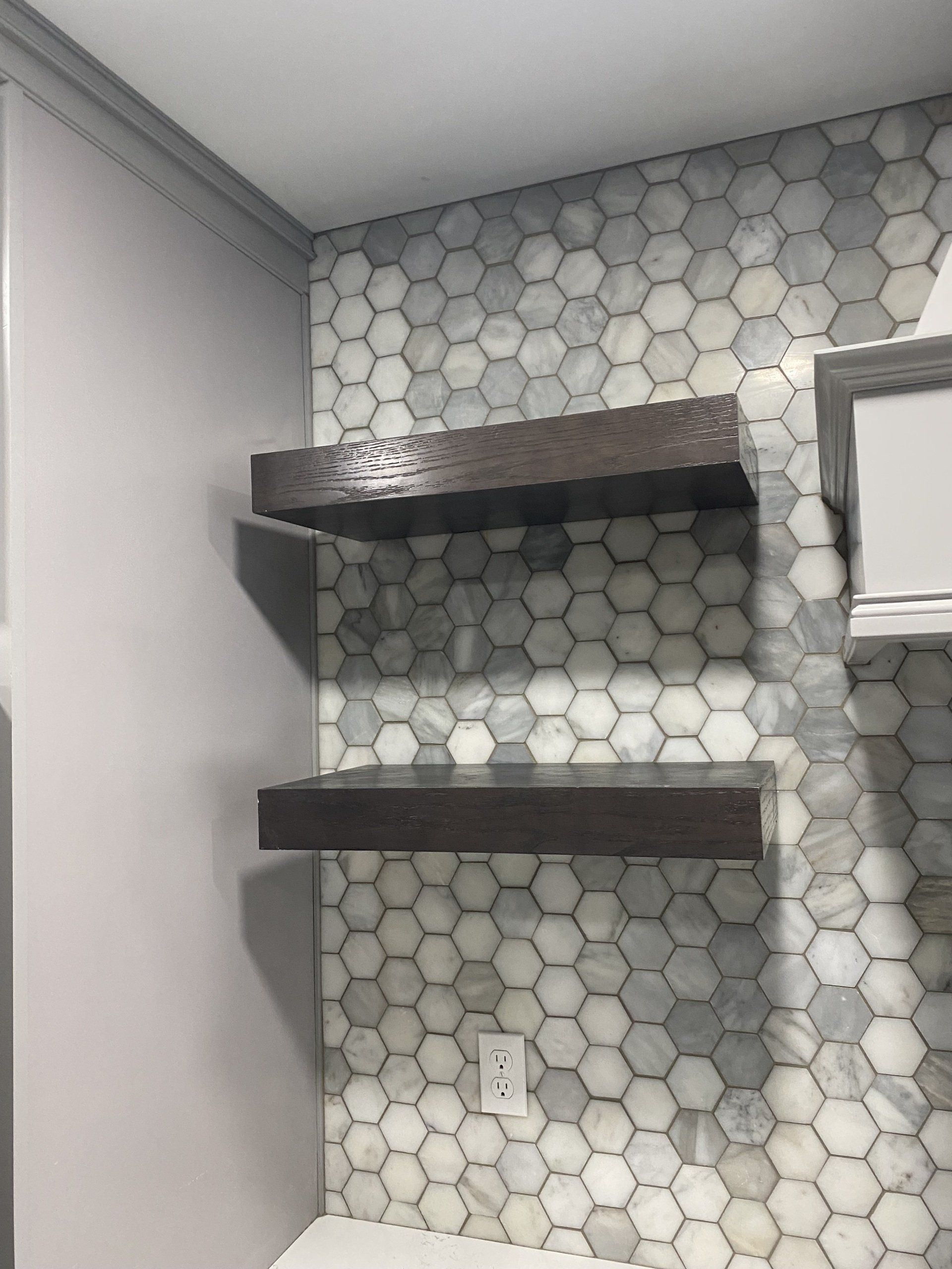 Two shelves are hanging on a wall in a bathroom.