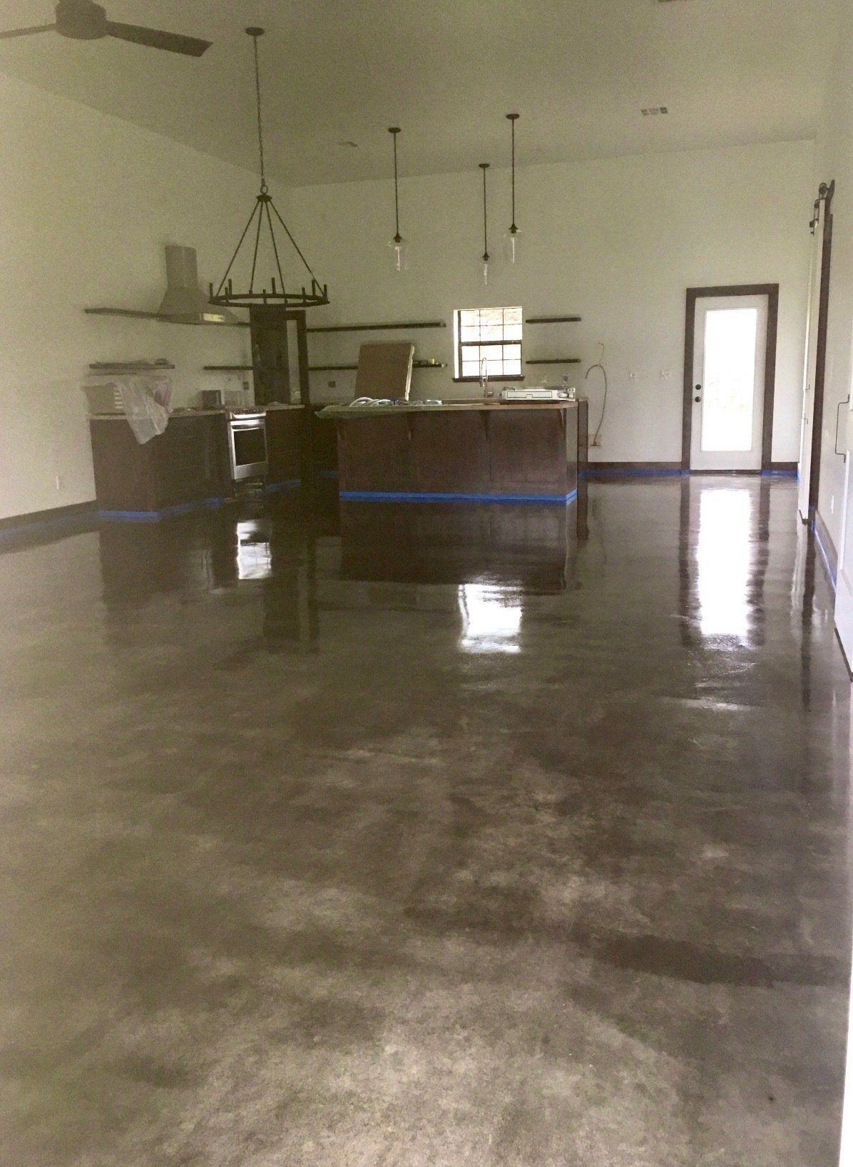 A large empty room with a ceiling fan and a kitchen in the background.