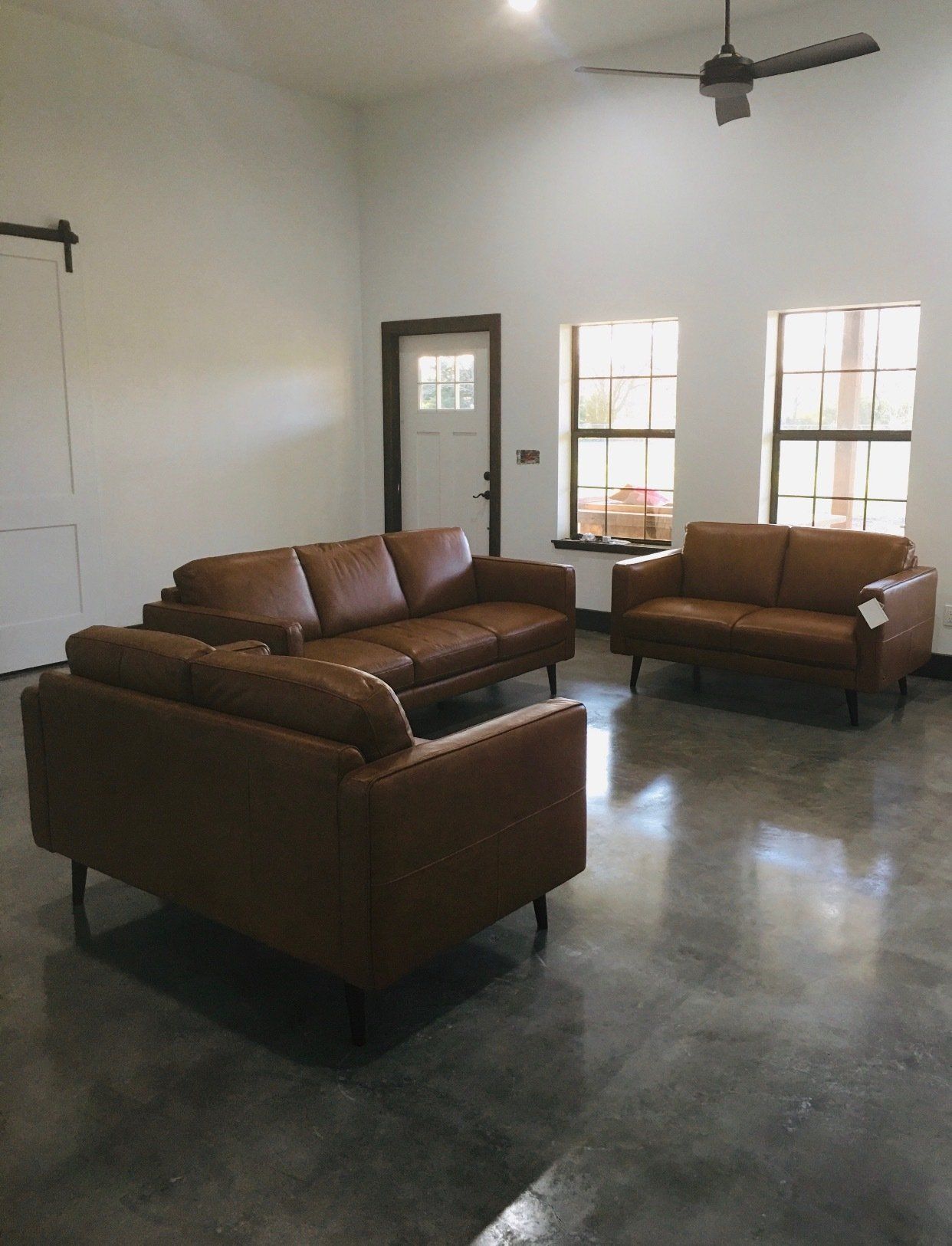 A living room with two brown leather couches and a ceiling fan.