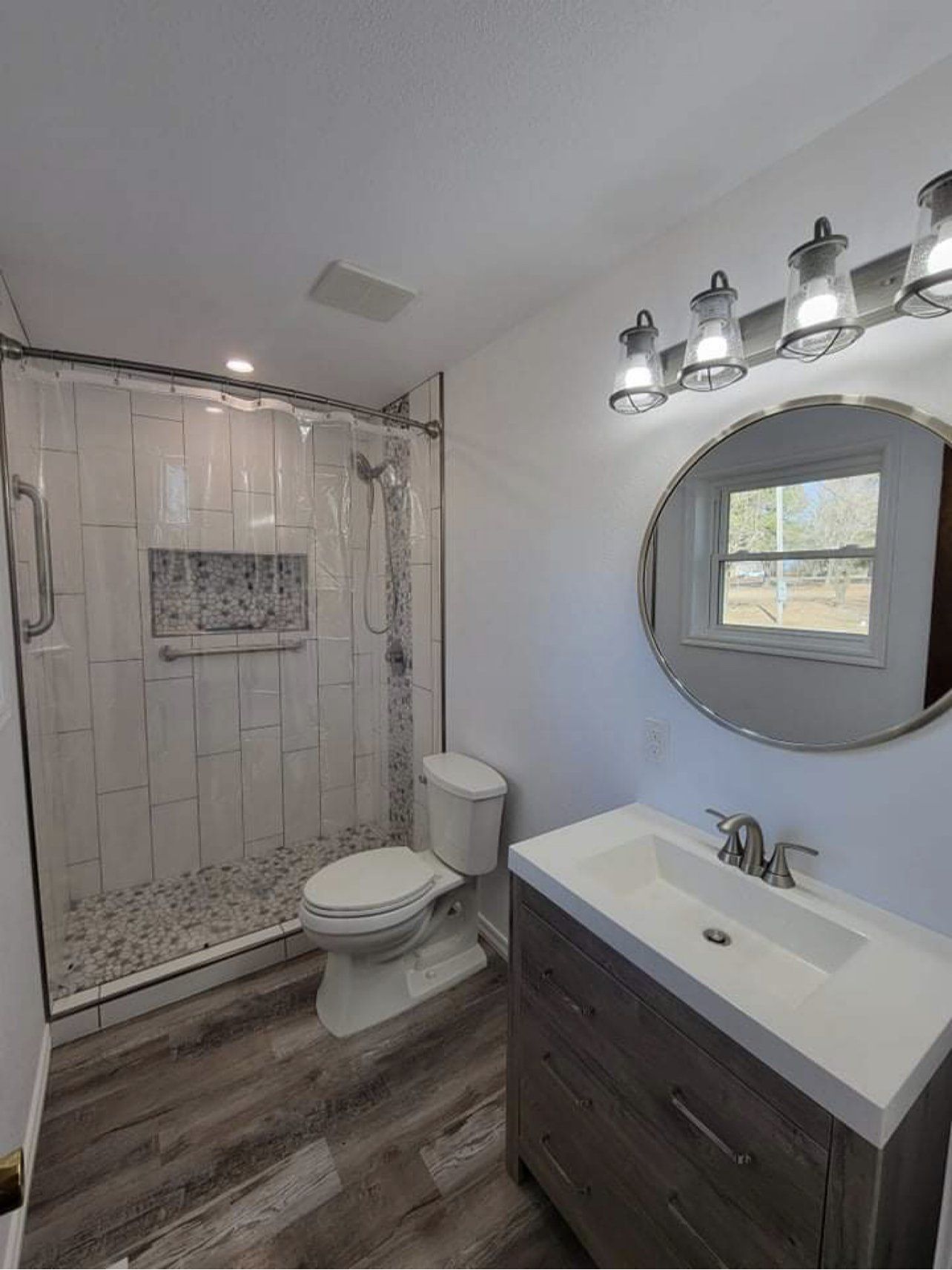A bathroom with a toilet , sink , shower and mirror.