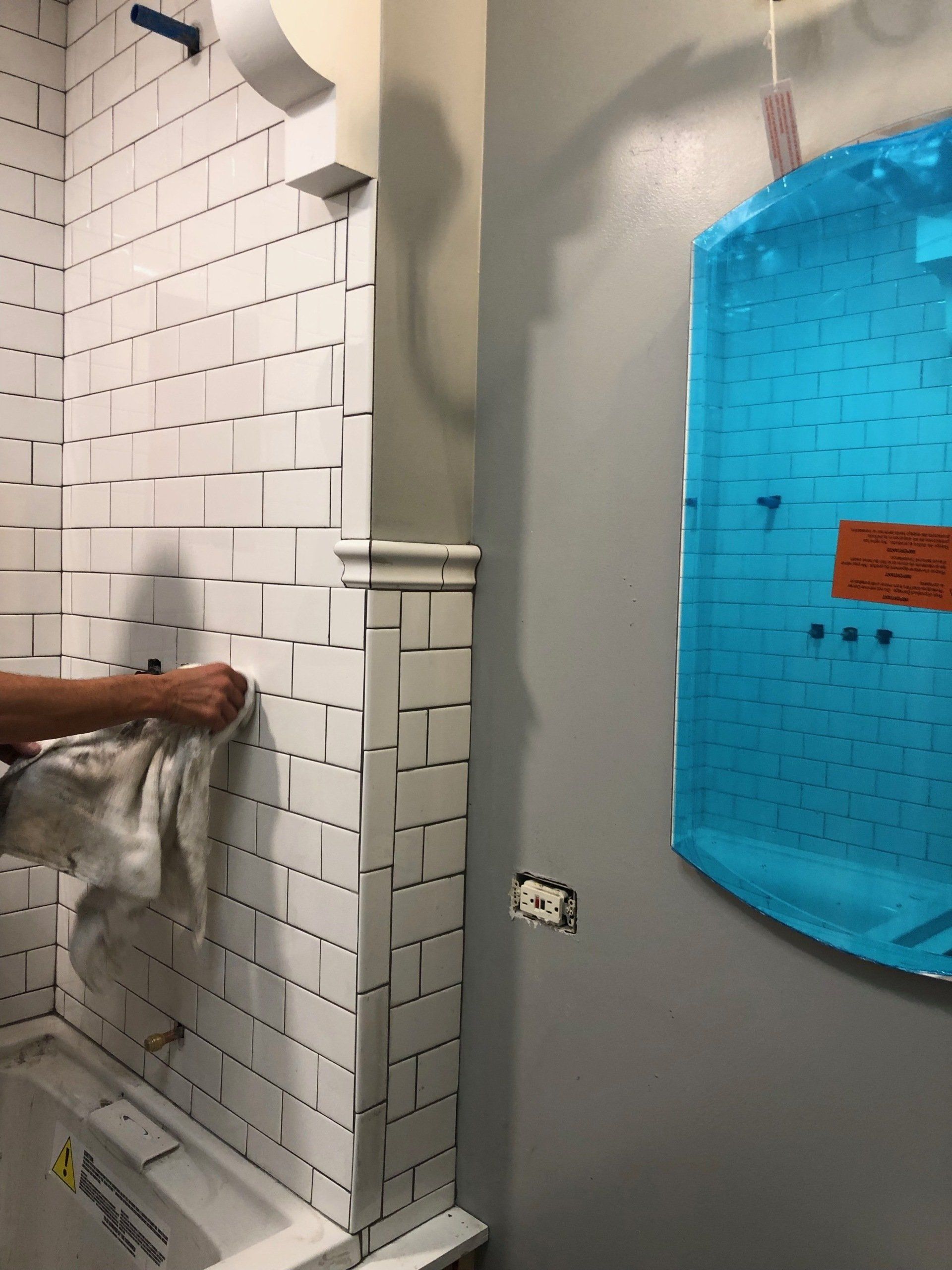A person is cleaning a bathroom wall with a towel
