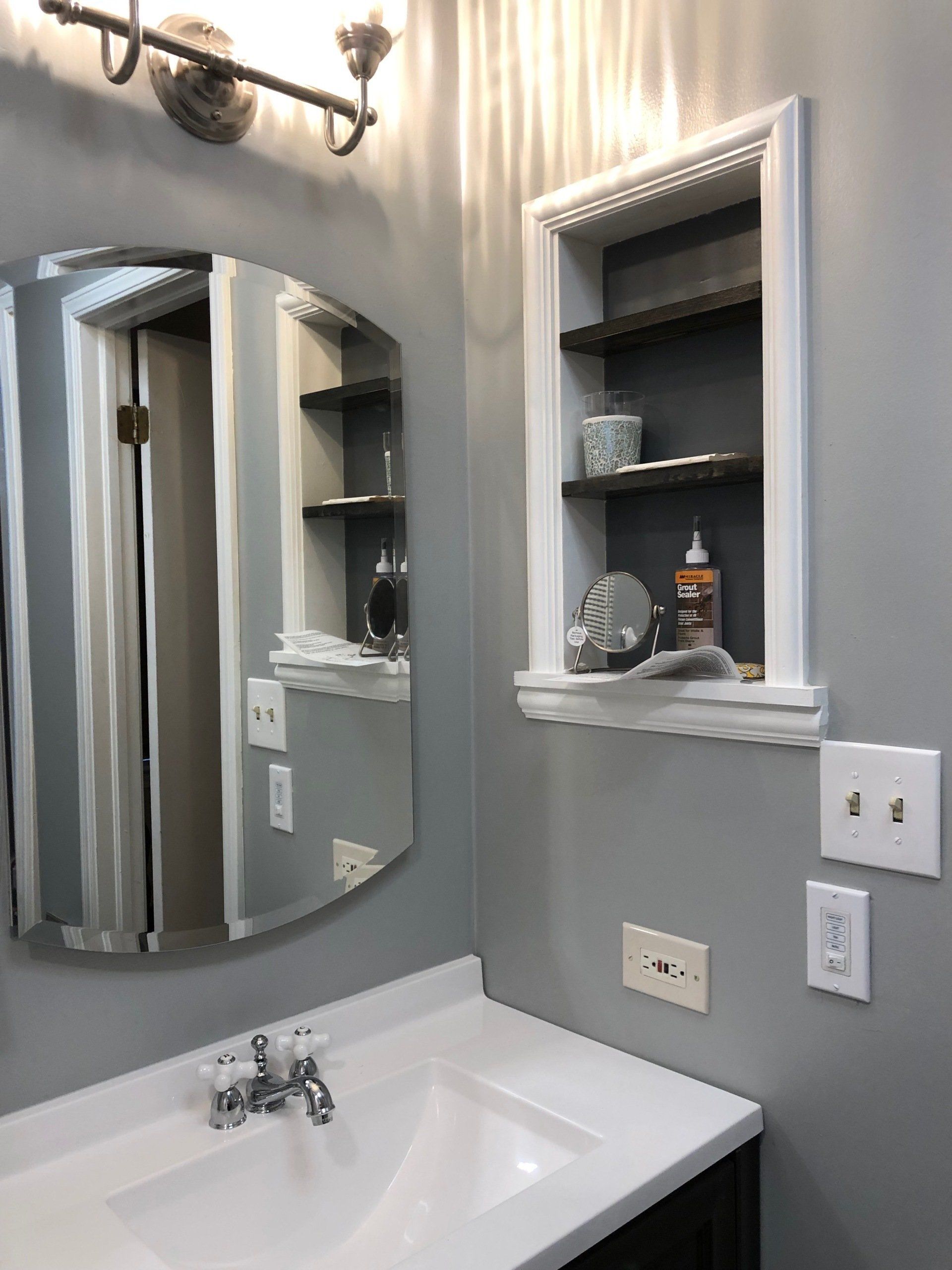 A bathroom with a sink , mirror and shelf.