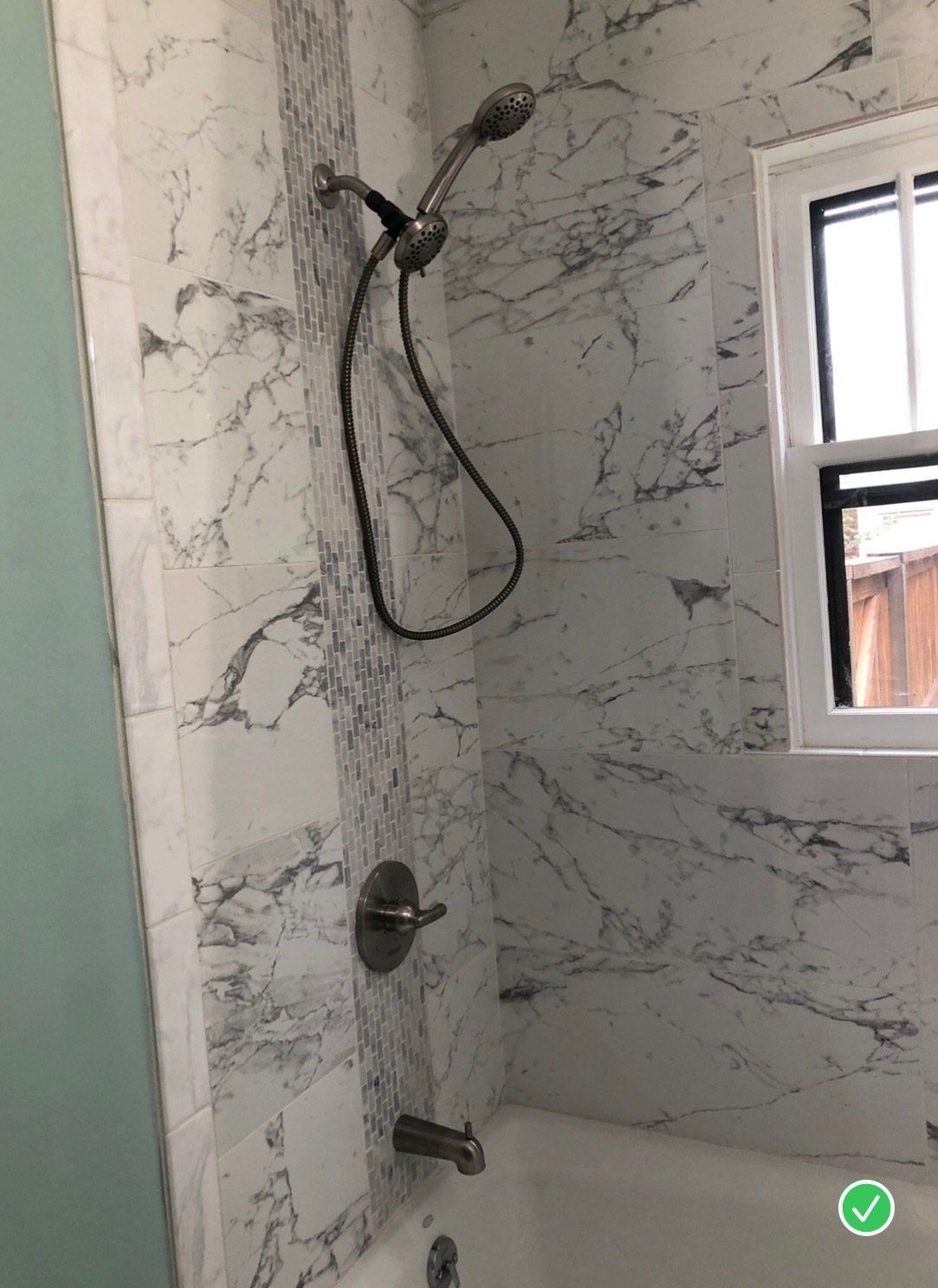 A bathroom with marble tiles , a tub and a shower head.