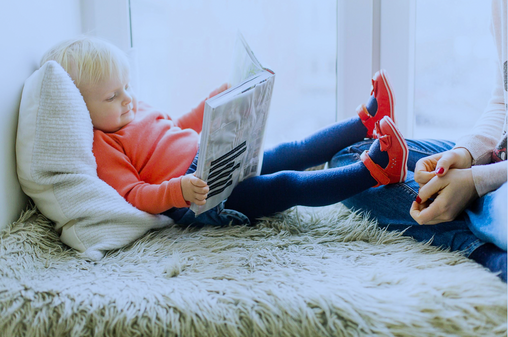 A little girl is laying on the floor reading a book.