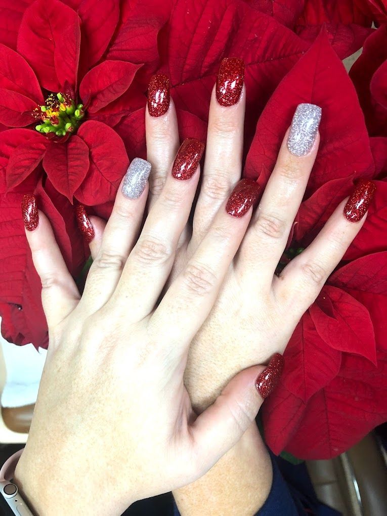 A woman 's hands with red and silver nails are holding a red flower.