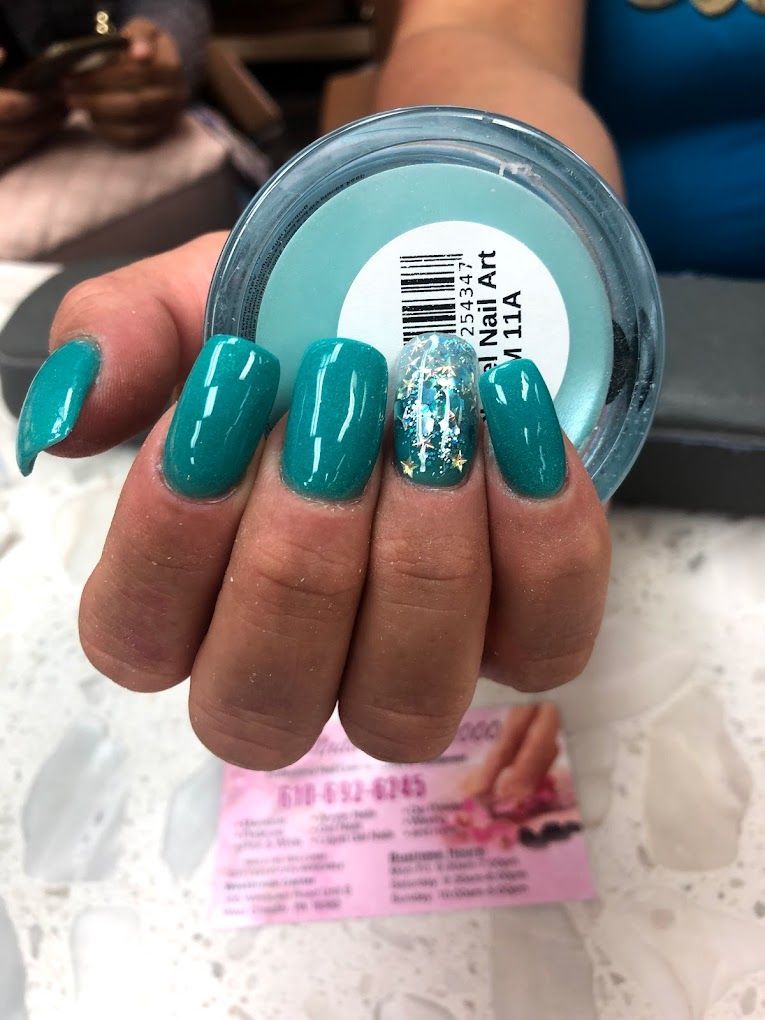 A woman 's nails are painted teal and she is holding a jar of nail art powder.