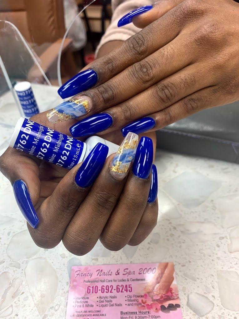A woman with long blue nails is holding a bottle of nail polish.