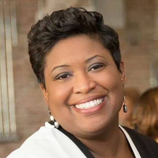 Woman with short dark hair, smiling broadly, wearing a black and white blazer.