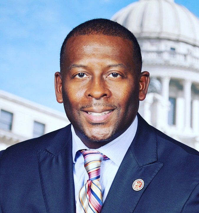 Man in a suit smiles, a building facade in the background.