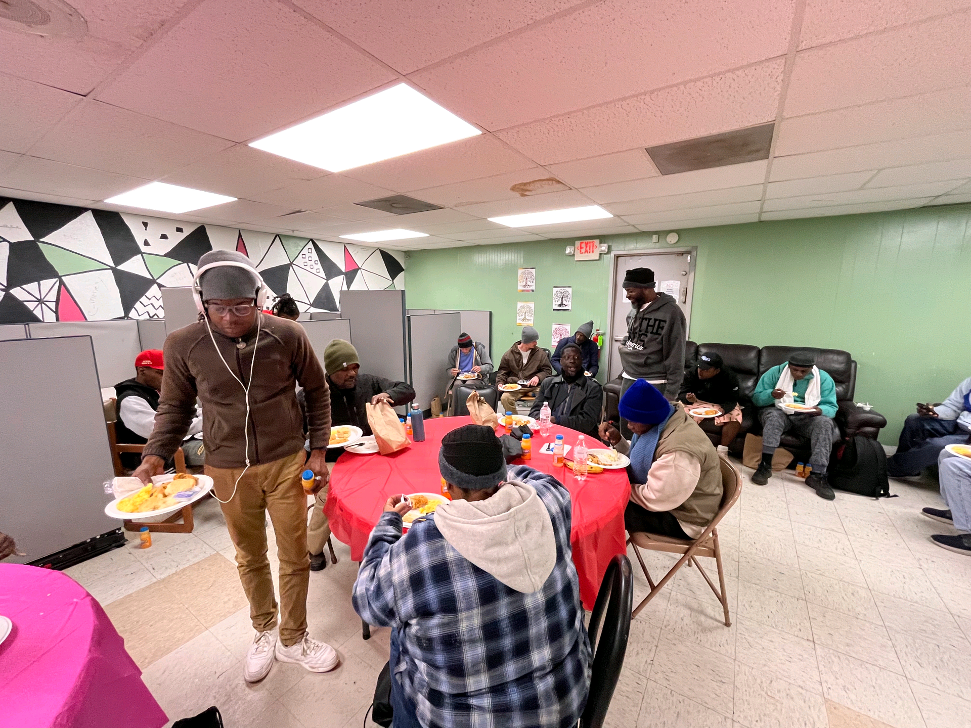 People eating and socializing at tables, served by a person with food. Room with colorful accents.
