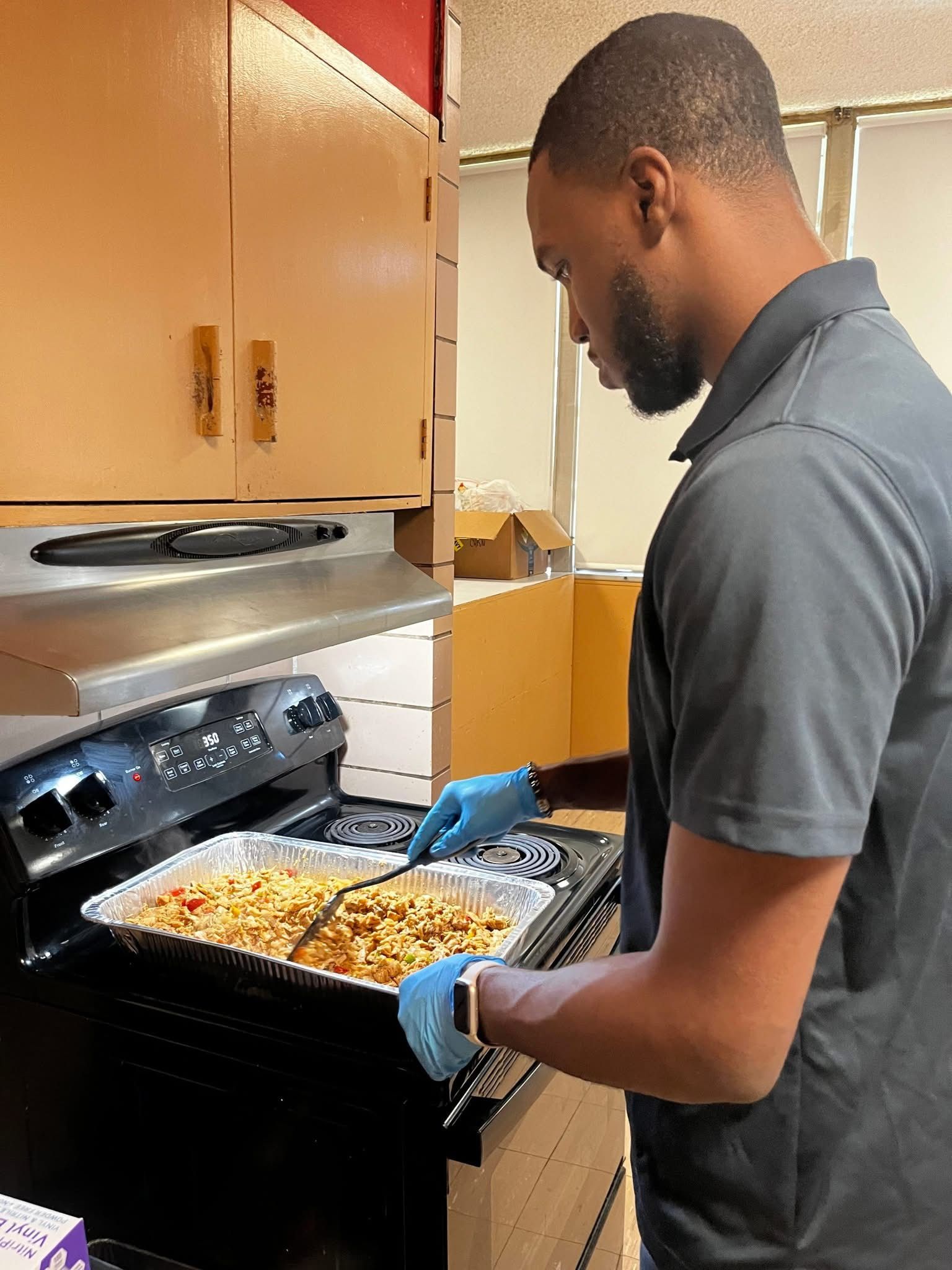 Man in a kitchen wearing gloves, stirring food on the stovetop.