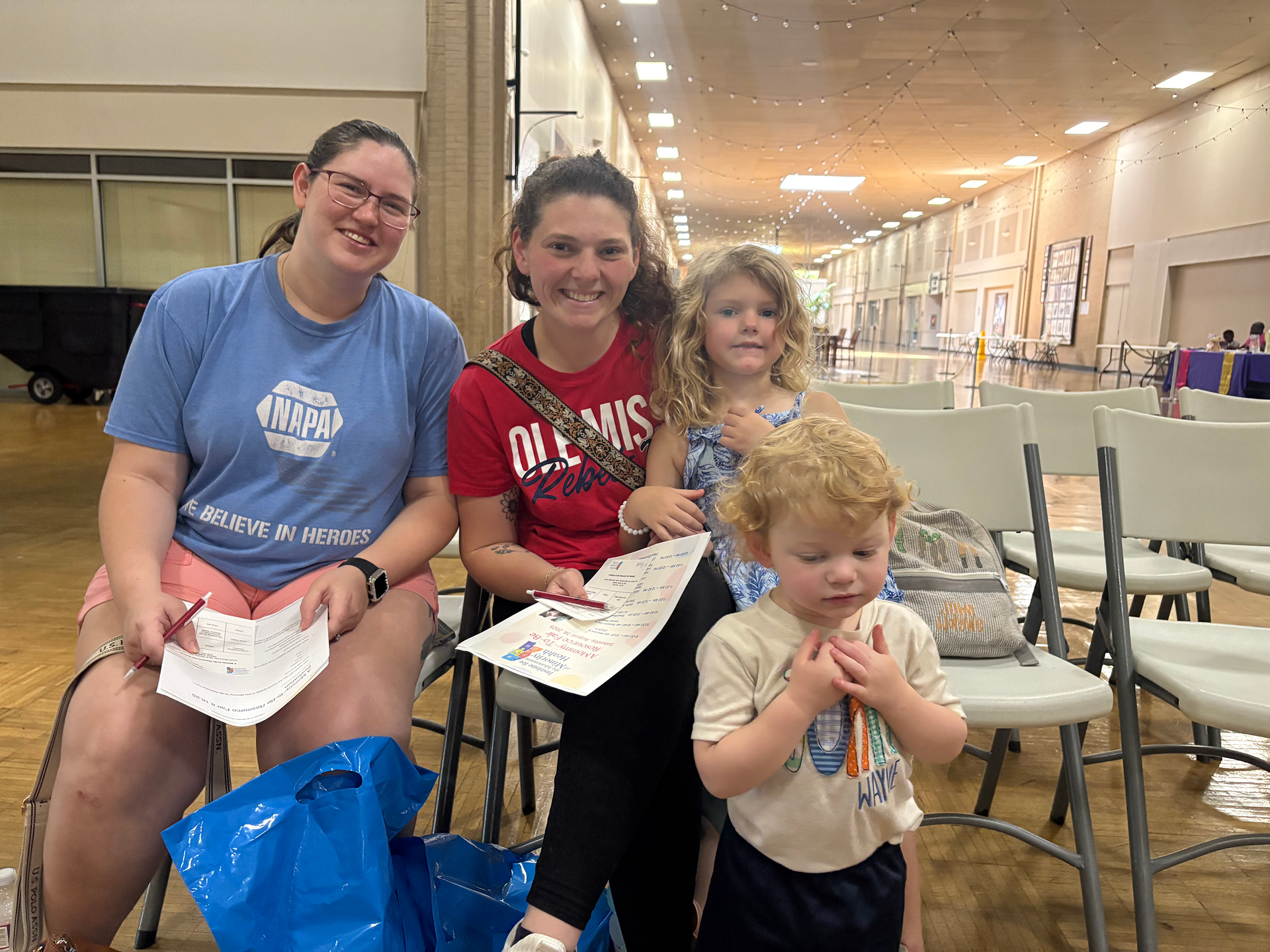 Doctor examining pregnant person's abdomen, smiling. Light-skinned person in pink shirt; setting appears to be a bedroom.