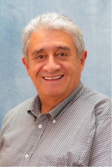 Smiling man with graying hair, wearing a patterned button-down shirt.