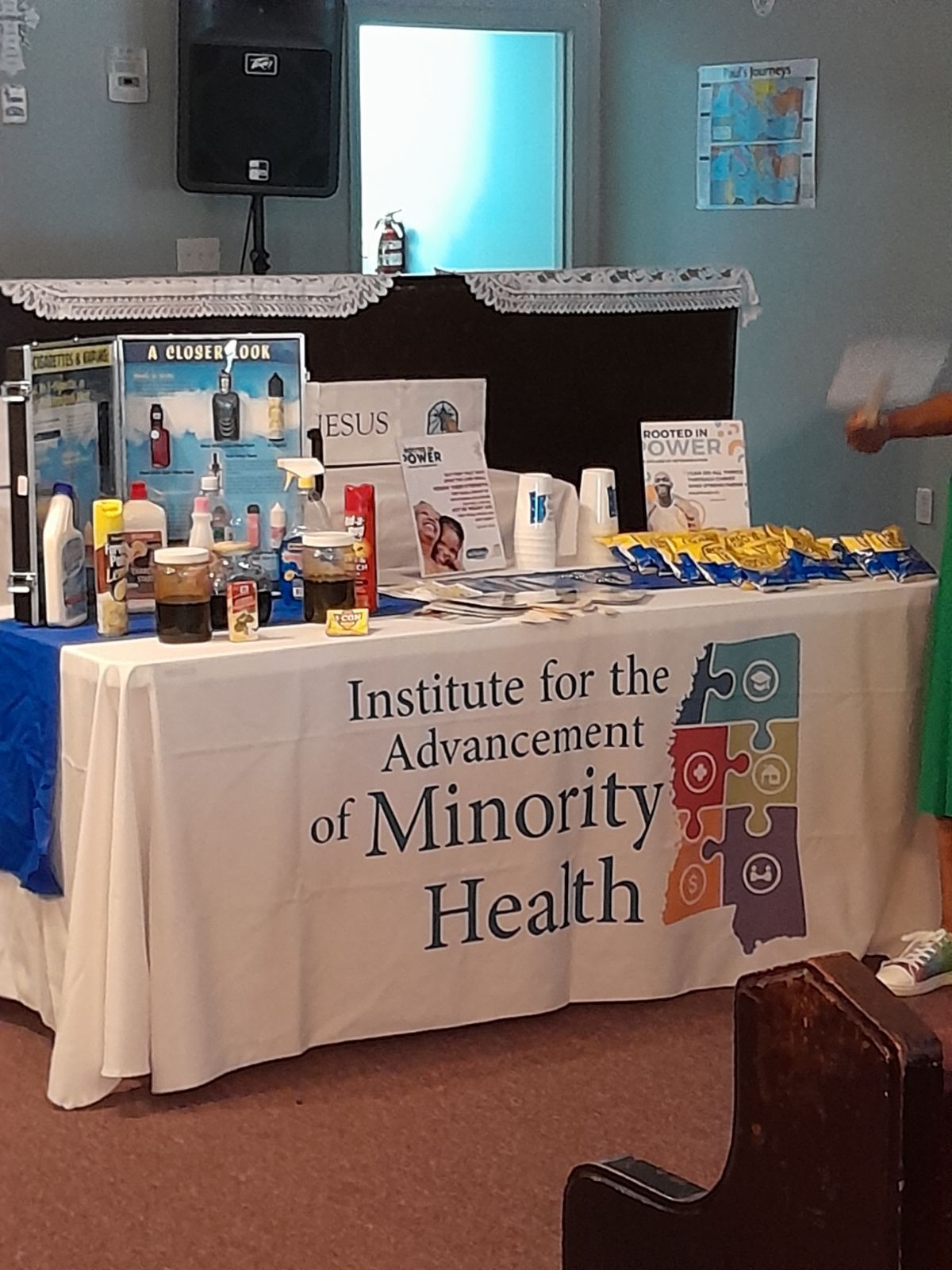 Institute for the Advancement of Minority Health table with brochures, products, and a person's arm, in a room.