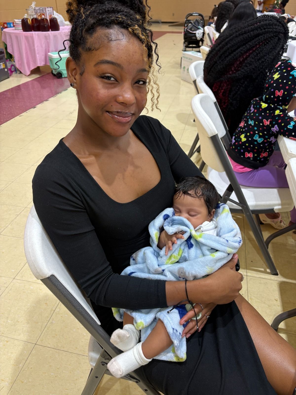Woman in black dress holding a sleeping baby in a blue blanket at a banquet hall.