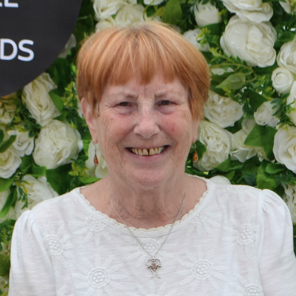 A woman with red hair is smiling in front of a wall of white flowers