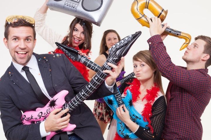 Group posing with colorful inflatable guitars and a boombox, smiling in a bright studio backdrop