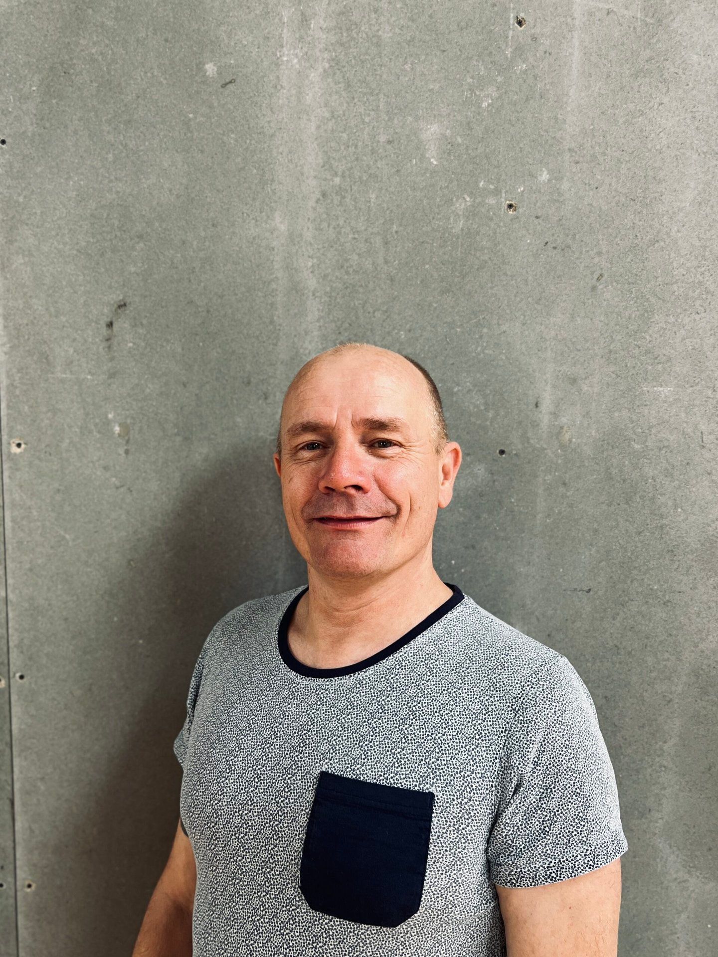 En mand i en grå skjorte smiler foran en grå væg.