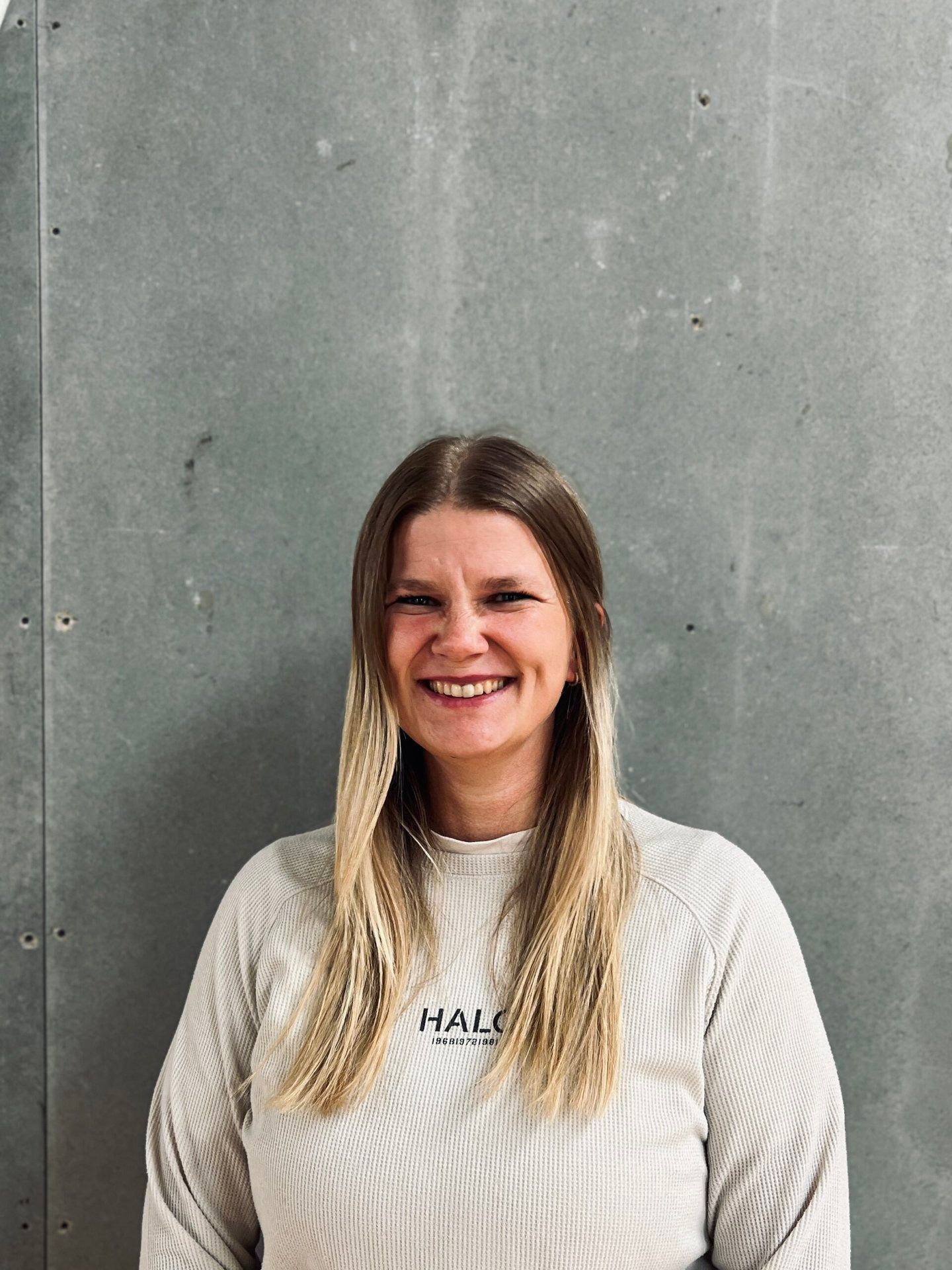 En kvinde i en hvid sweater smiler foran en grå væg.