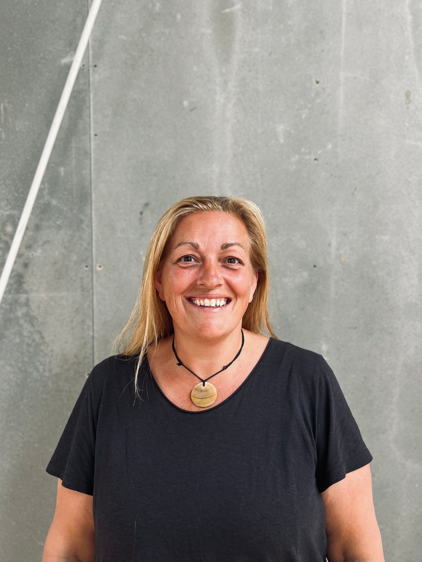 En kvinde iført en sort skjorte og en halskæde smiler til kameraet.