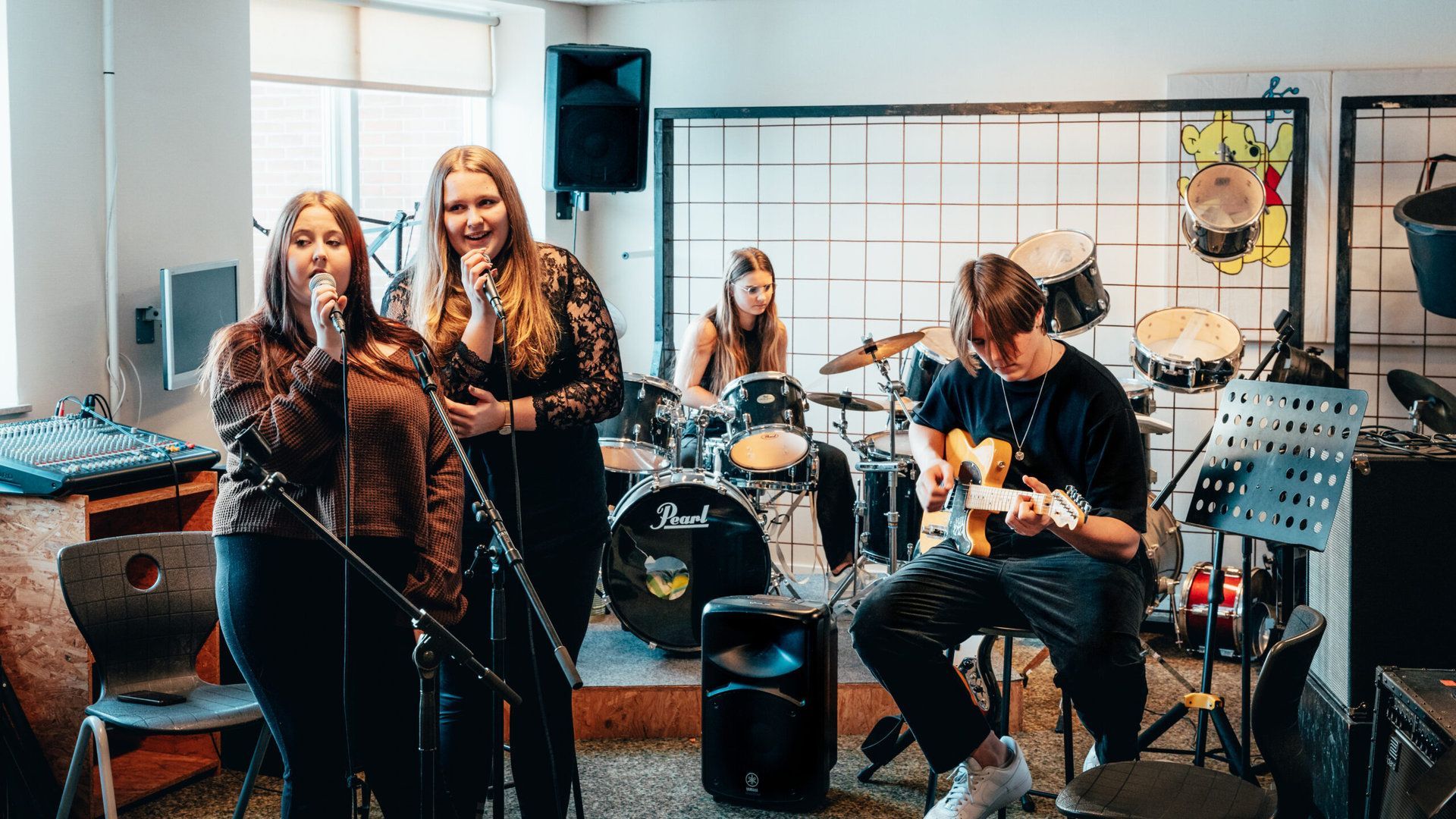 En gruppe unge mennesker synger og spiller på instrumenter i et rum.