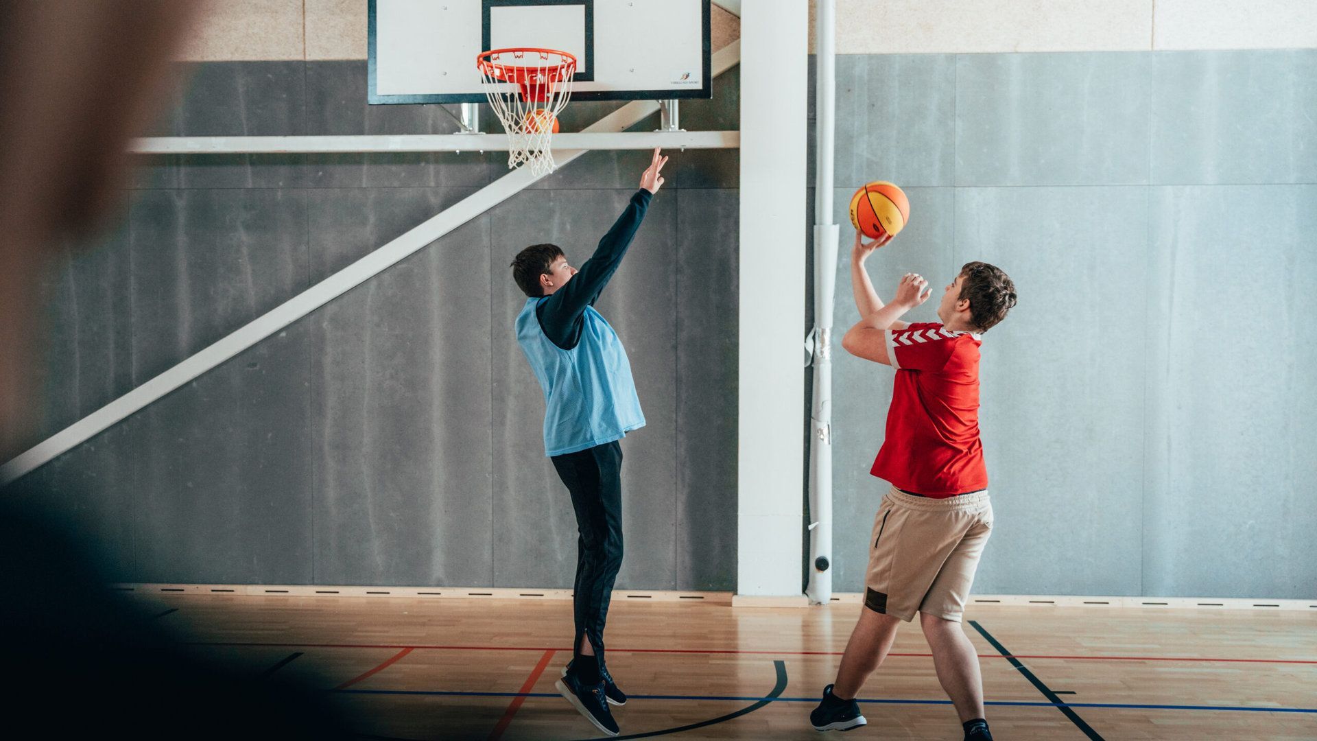 To unge mænd spiller basketball i en sportshal.