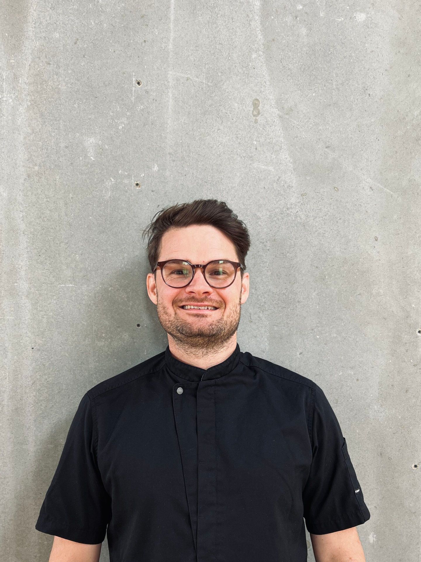 En mand iført briller og en sort skjorte smiler til kameraet.