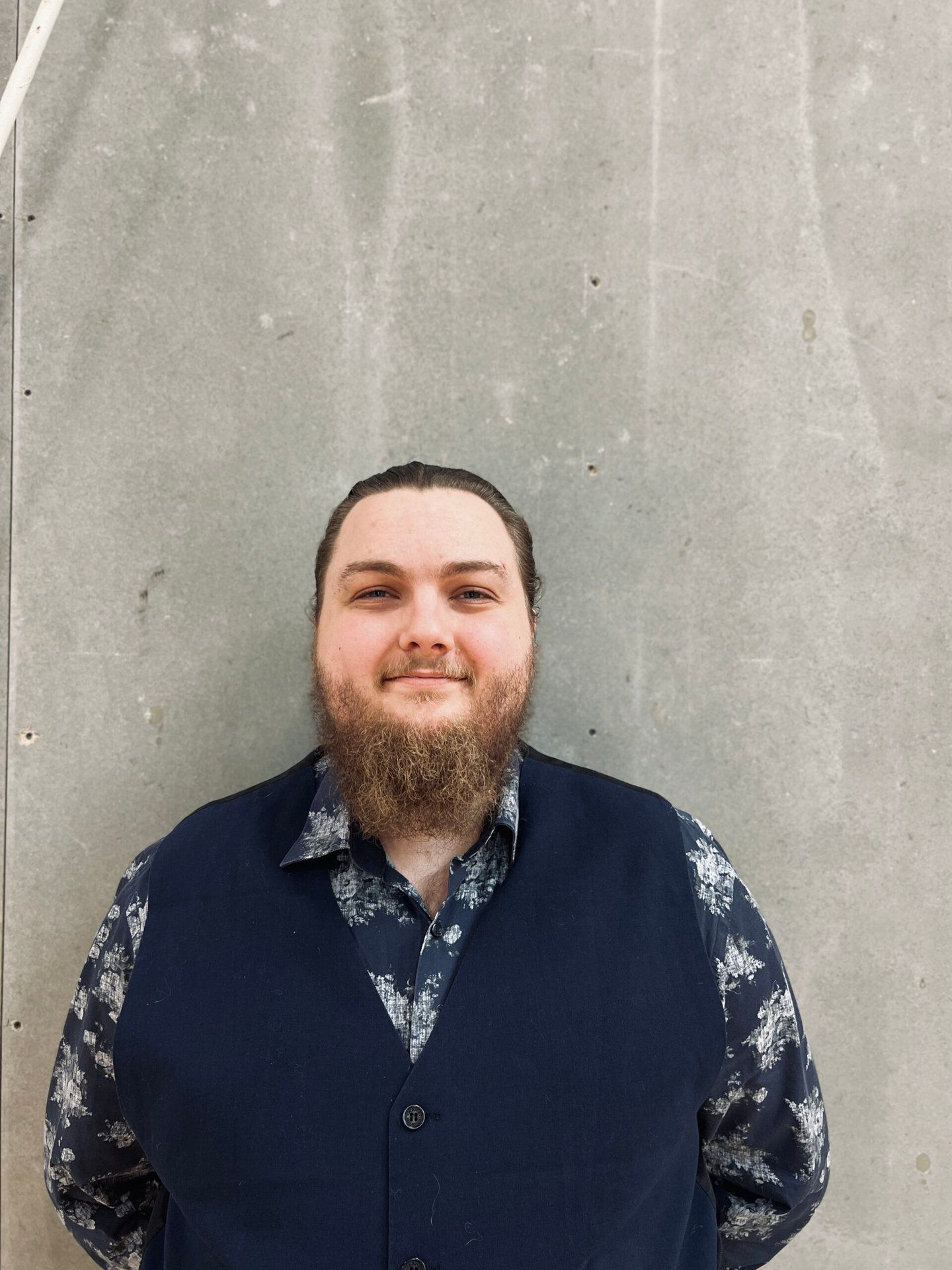 En mand med skæg er iført en blå vest og en blomstret skjorte.