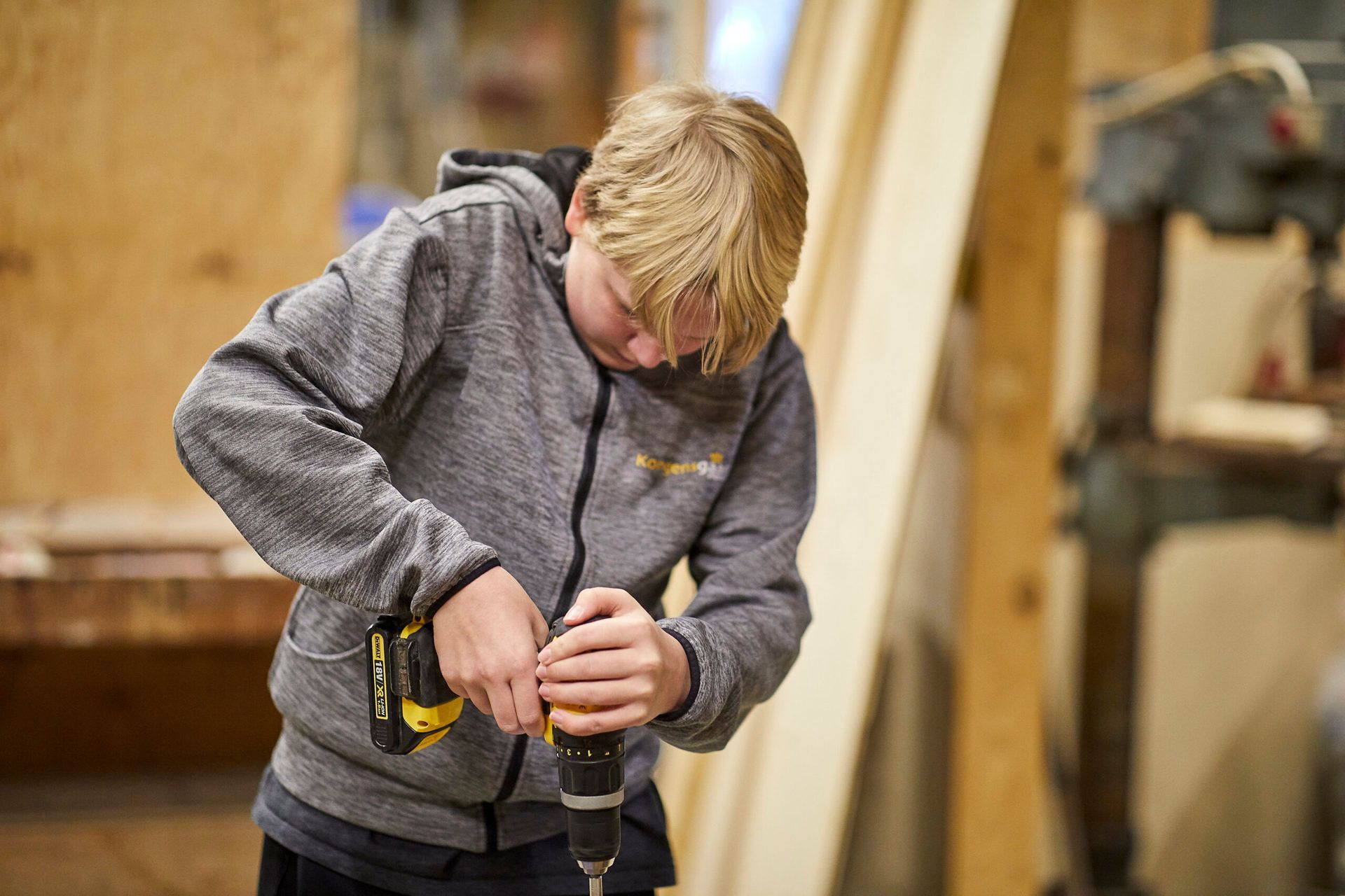 En ung dreng bruger en boremaskine til at bore et hul i et stykke træ.