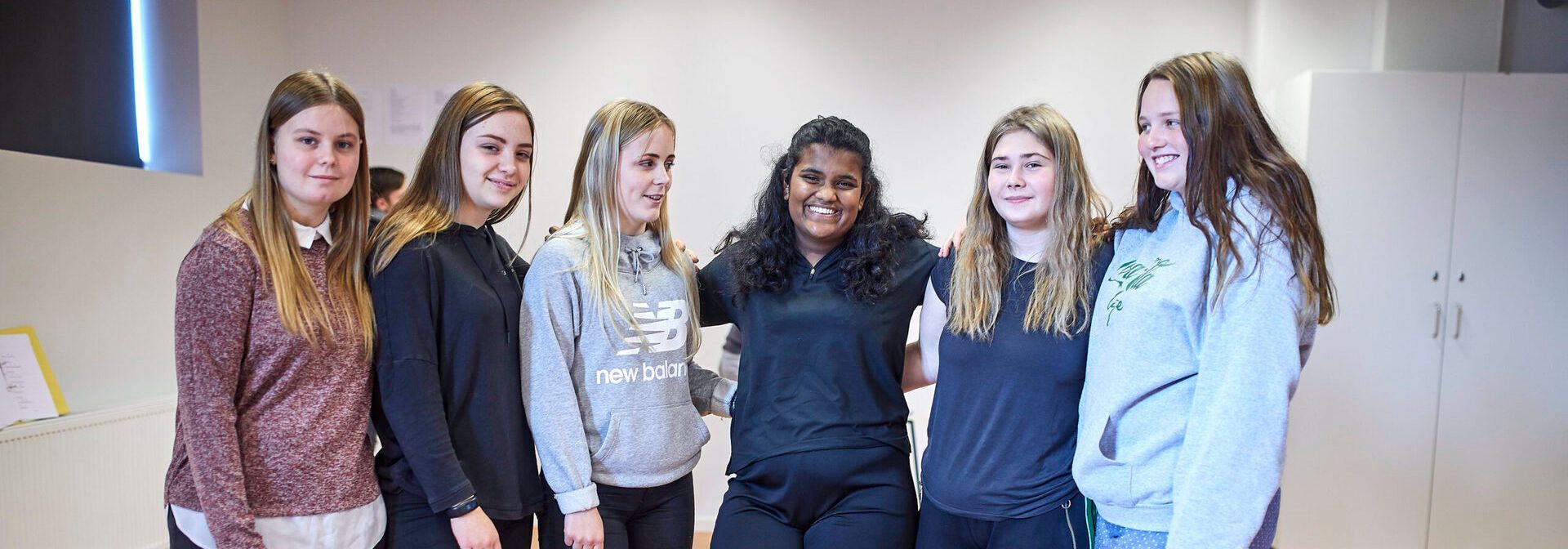 En gruppe unge kvinder stiller op til billede sammen i et værelse.