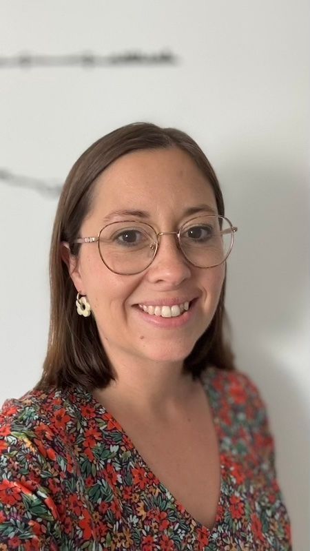 Une femme portant une veste rayée et une chemise noire sourit à la caméra.