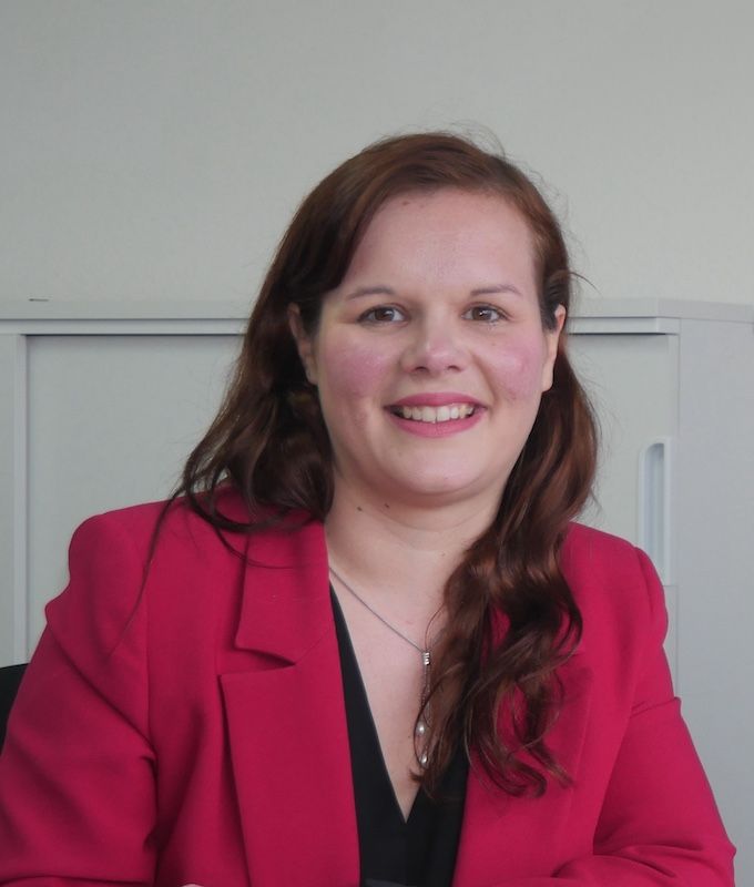 Une femme aux cheveux bouclés porte un pull vert et sourit.