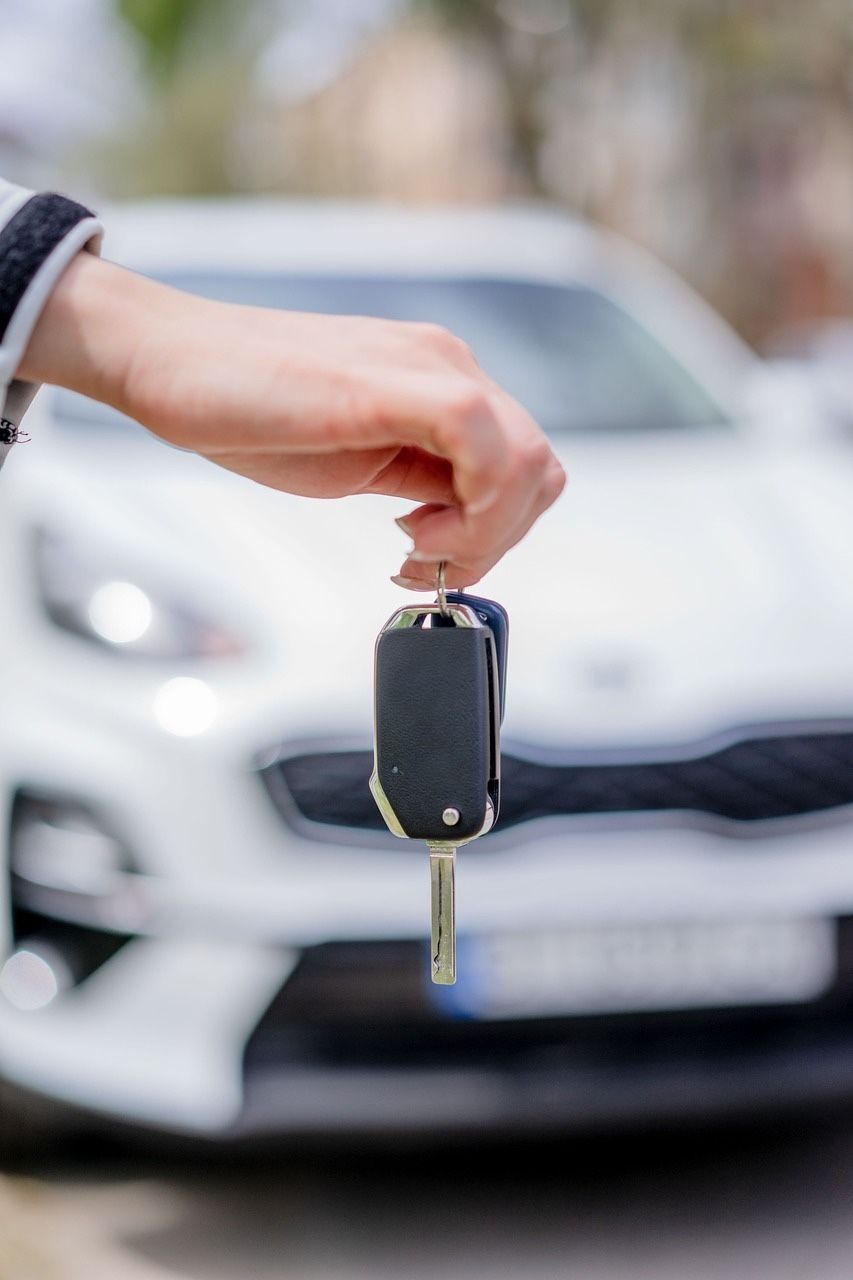 Une personne tient une clé de voiture devant une voiture blanche.