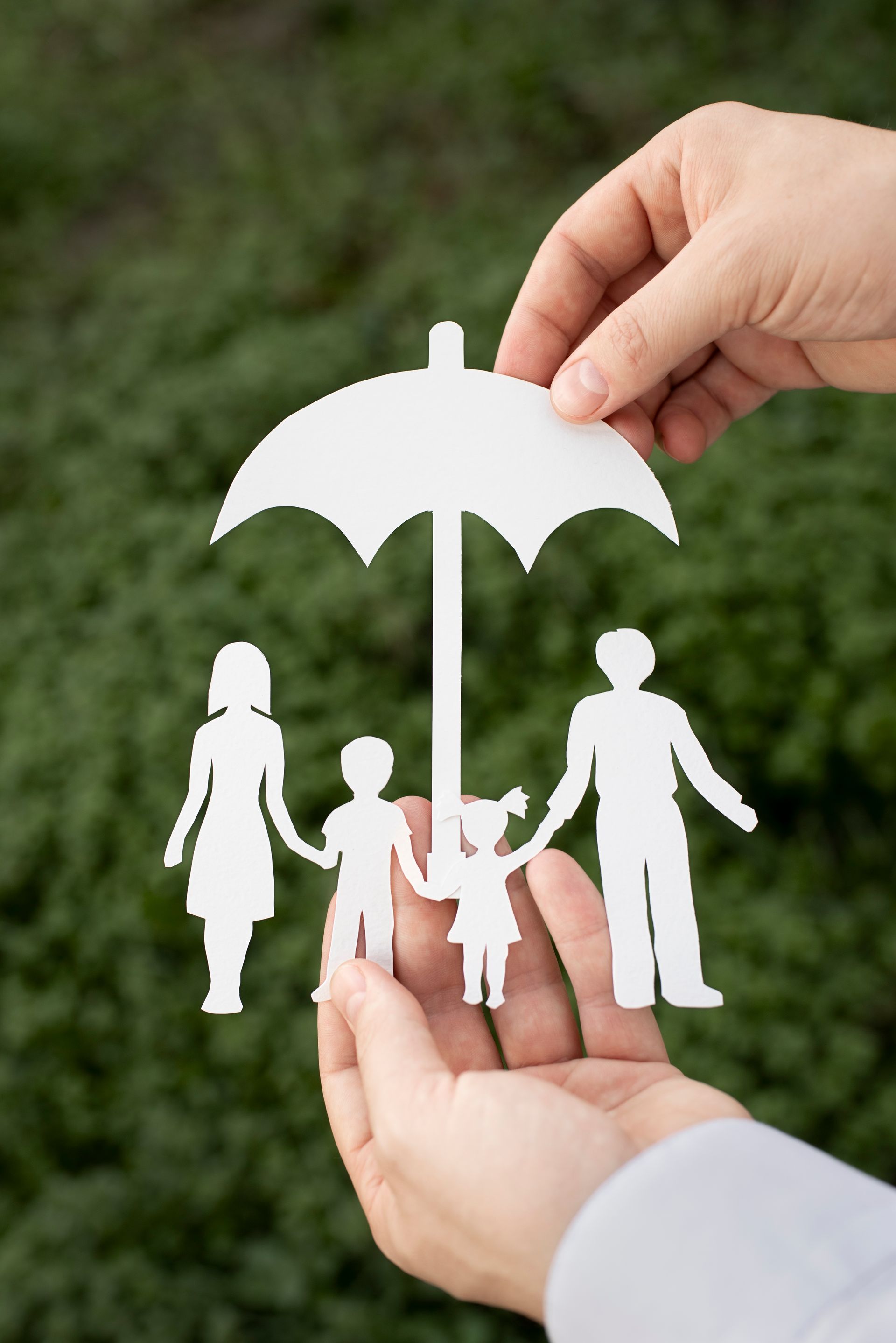 Une personne tient un papier découpé représentant une famille sous un parapluie.