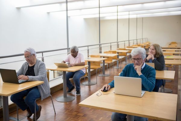 A group of people are sitting at tables in a room with a clock on the wall