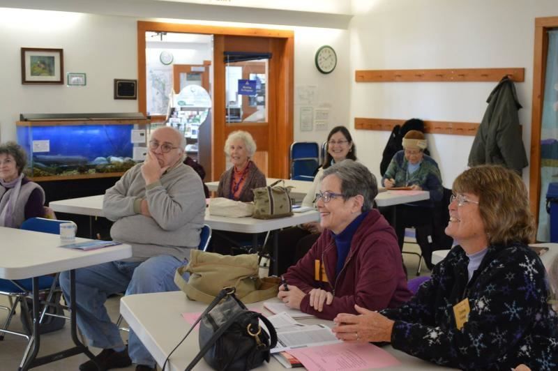 A group of people are sitting at tables in a room with a clock on the wall