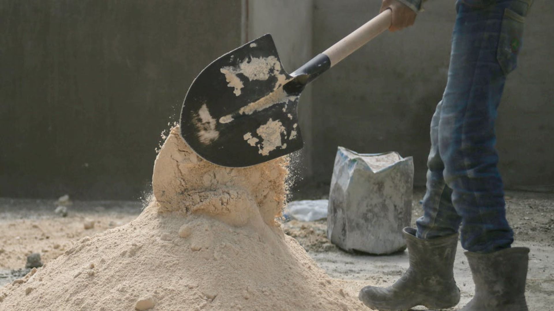 Una persona sostiene una pala sobre un montón de arena.