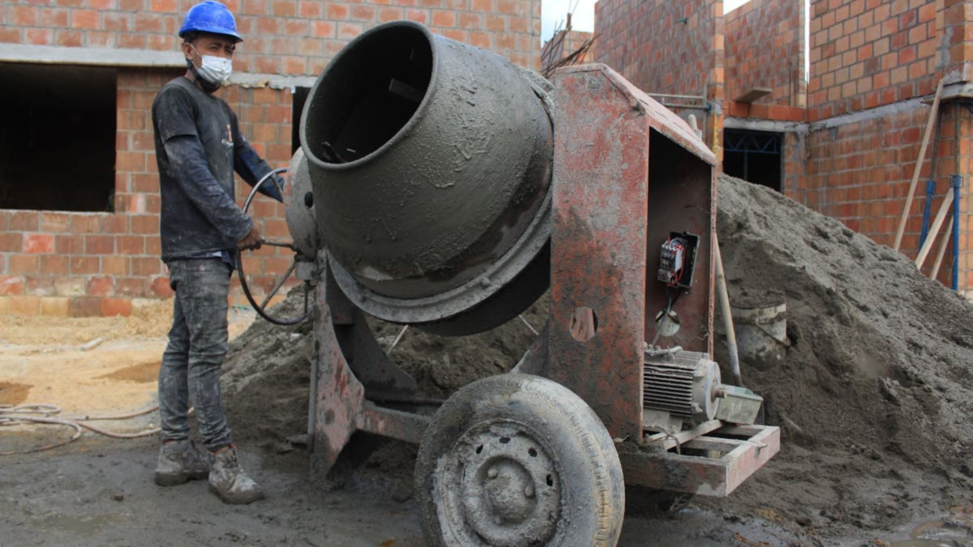 Un hombre está de pie junto a una hormigonera en un sitio de construcción.