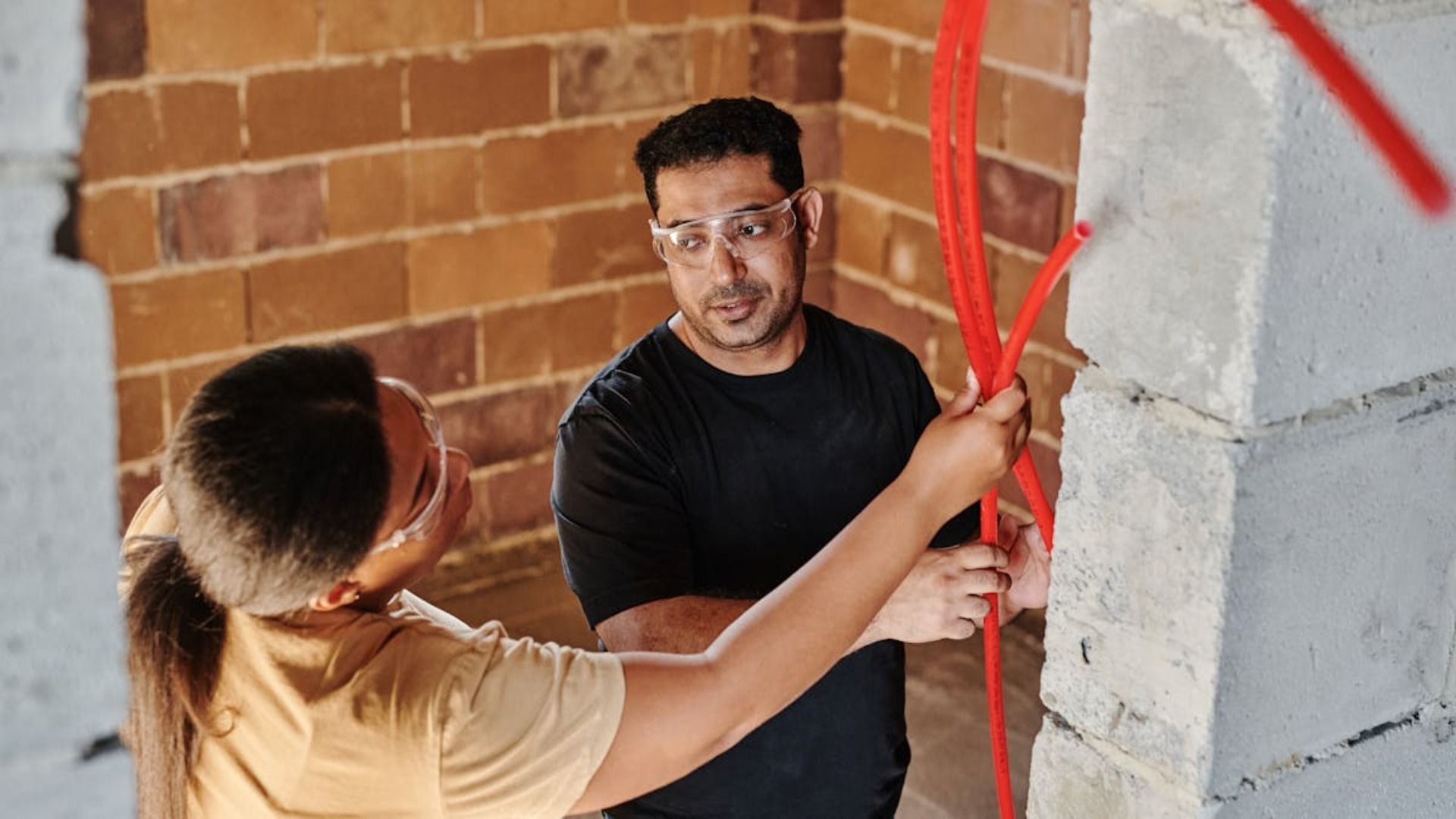 Un hombre y una mujer están midiendo una pared de ladrillos con una cinta métrica.