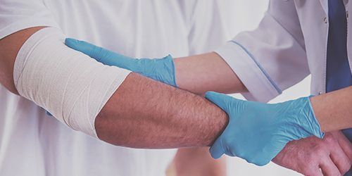 Un médecin bande le coude d'un patient avec un bandage.